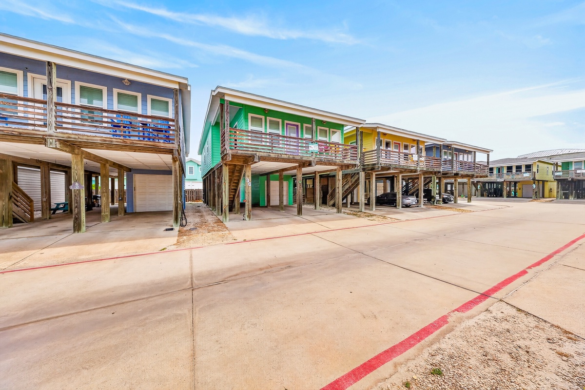 A row of elevated beach cottages features bright, colorful exteriors and covered parking beneath each unit. These stilt homes sit within a peaceful coastal community.