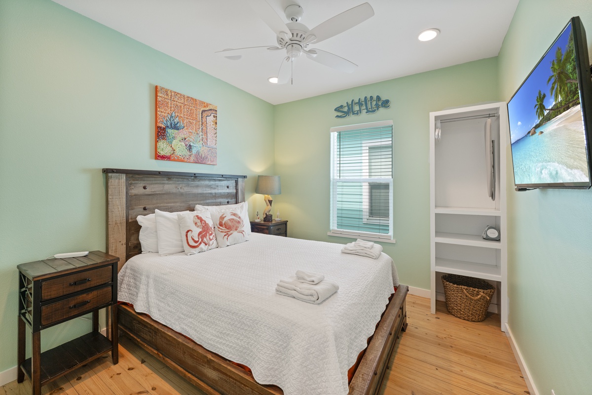 Slip into your serene coastal retreat where soft seafoam walls and charming beach décor invite you to unwind. Your cozy bed awaits beneath a gentle ceiling fan, with fresh towels and everything you need for a restful stay.