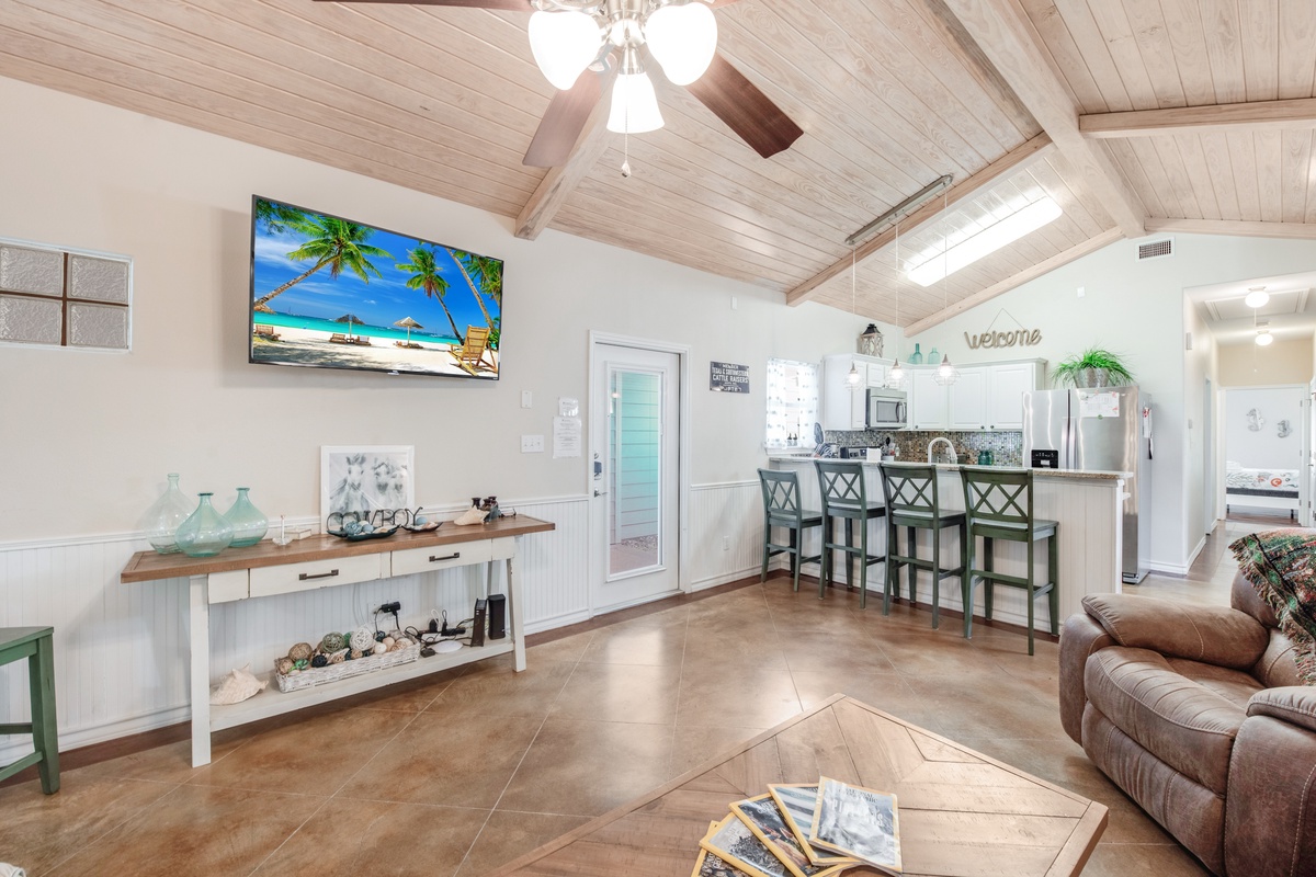 Relax in your open-concept living space featuring vaulted ceilings, coastal décor, and a fully equipped kitchen with breakfast bar.