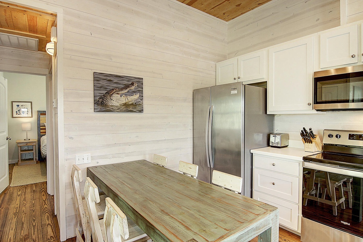 Your bright coastal kitchen features rustic wood paneling, modern appliances, and a weathered dining table perfect for morning coffee and meal prep.
