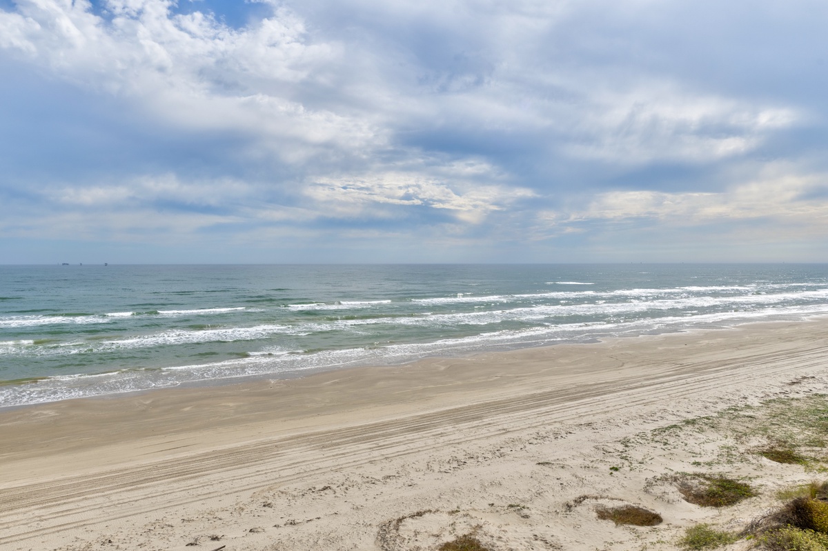 Pristine sandy beach stretches along the coastline with gentle waves and dramatic cloudy skies overhead.
