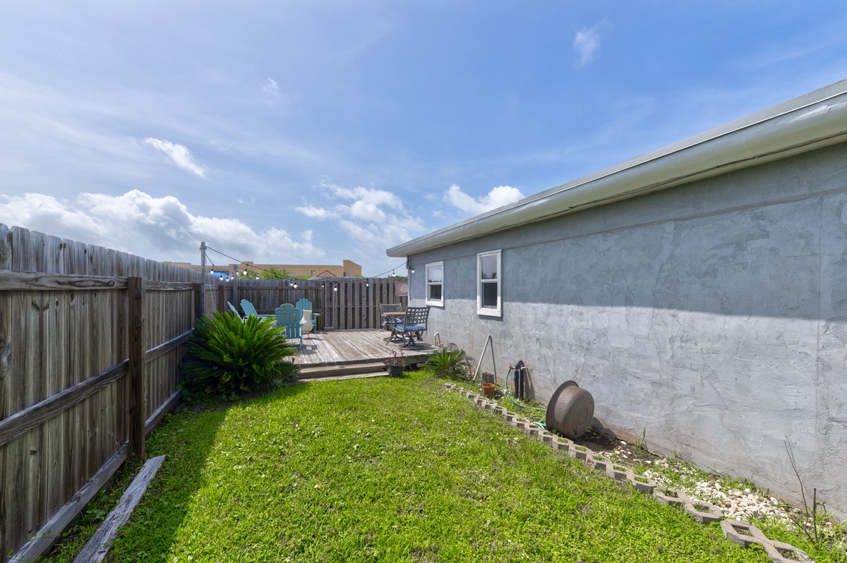 Modern home with private backyard featuring a sunny lawn and raised wooden deck with seating, enclosed by tall privacy fencing. Charming yard for relaxing outdoors in seclusion.