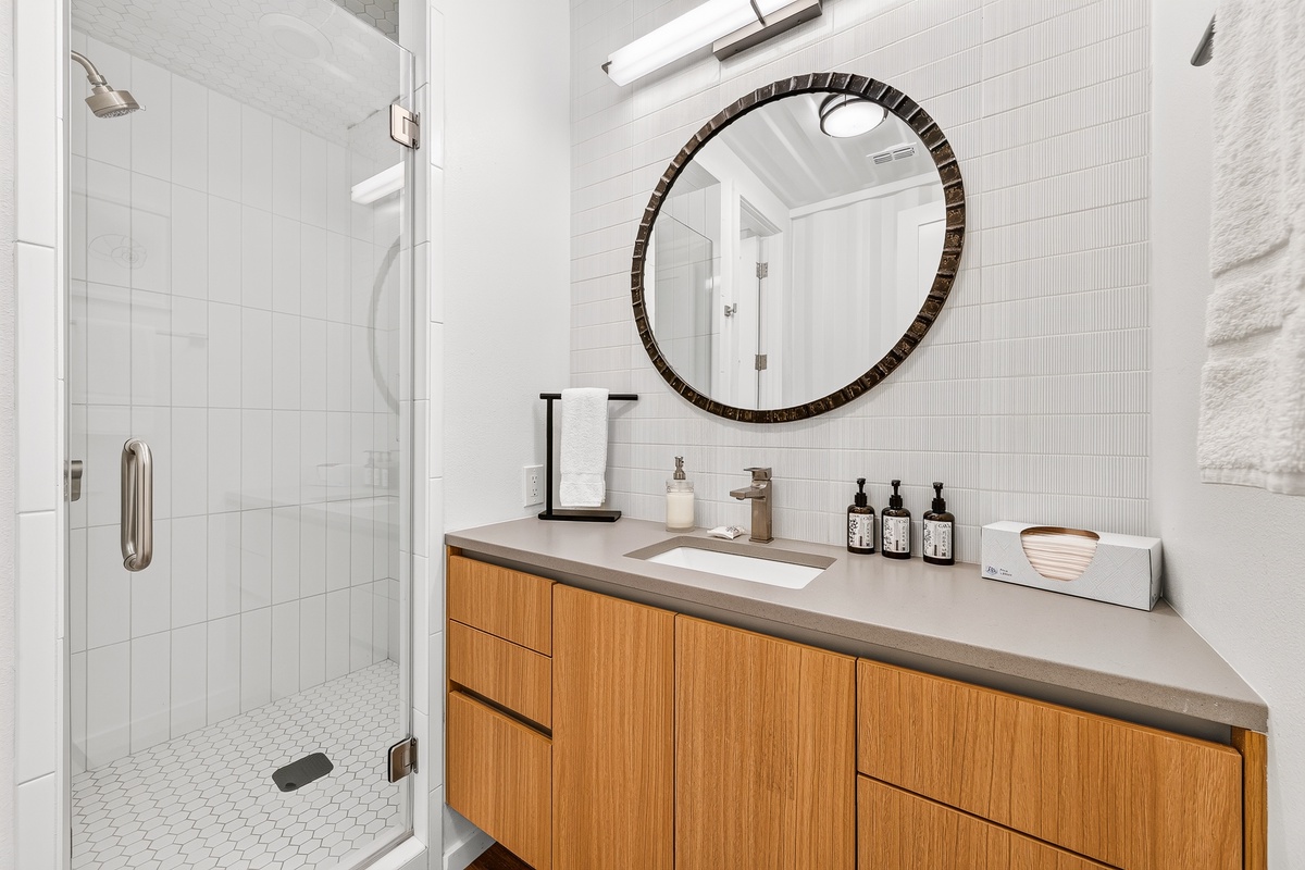 Step into your bright, private bathroom with a sleek glass shower, warm wood vanity, and stylish round mirror. Fresh towels and thoughtful amenities await—your perfect retreat after a day of adventure.