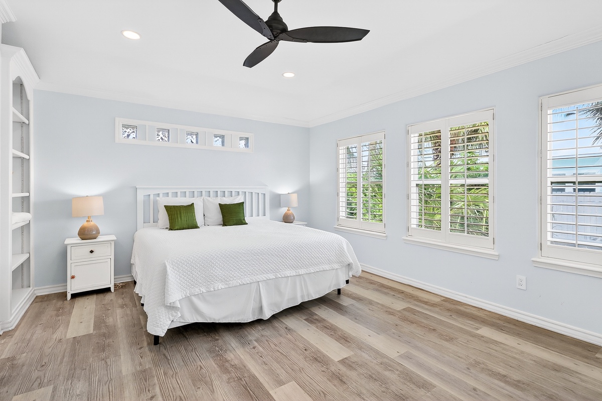 Drift off peacefully in your serene bedroom featuring crisp white linens, gentle ceiling fan breeze, and natural light streaming through plantation shutters.