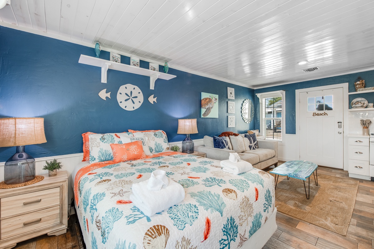 Drift off in your beach-themed bedroom featuring ocean-blue walls, coral accents, and cozy seating area perfect for morning coffee.