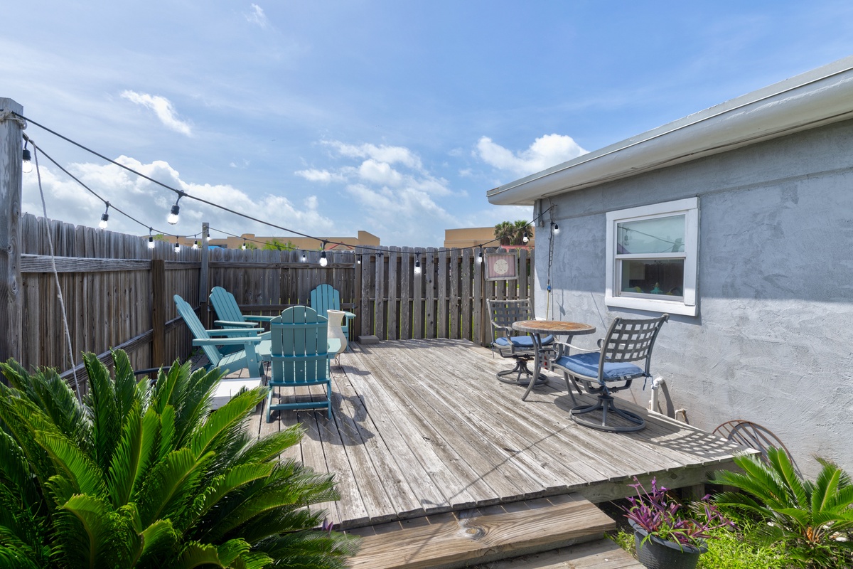 Your private deck awaits with teal Adirondack chairs, string lights overhead, and tropical greenery framing your perfect spot to unwind under sunny skies.