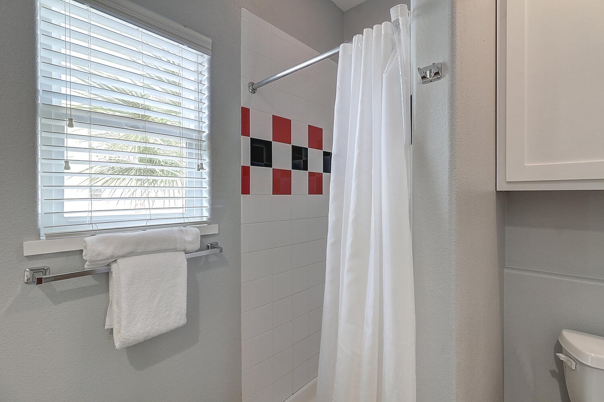 Step into your private bathroom with crisp white linens and cheerful red accents, where natural light streams through blinds for a bright, refreshing start to your day.