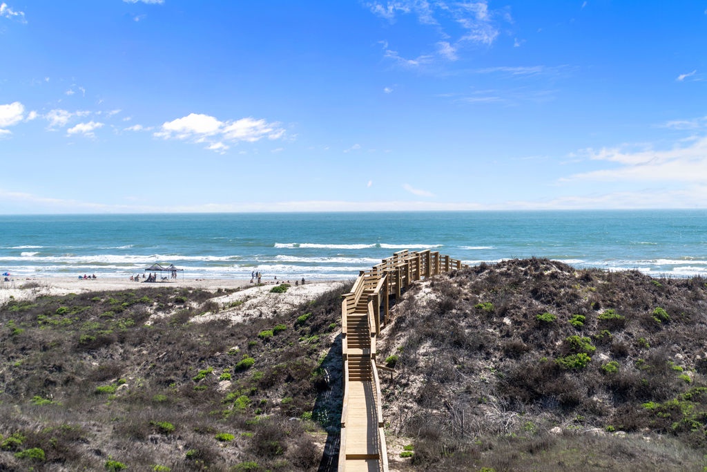 Coastal boardwalk leads through natural dunes to pristine beach access with ocean views and beach activities nearby.