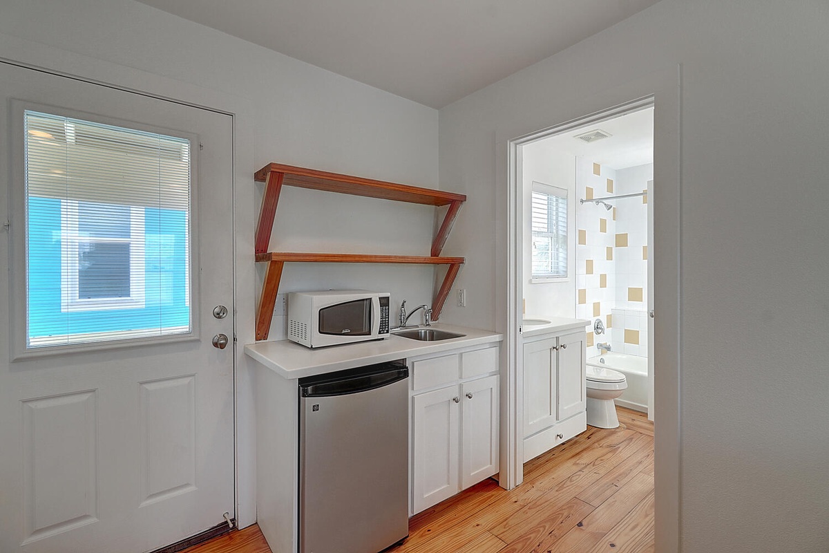 Your compact kitchenette has everything you need—microwave, mini-fridge, and sink with warm wood shelving above for your convenience.