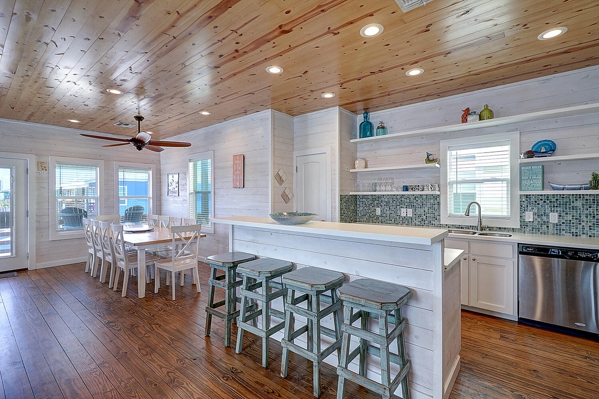 Your dream coastal kitchen awaits with warm wood ceilings, spacious island seating, and ocean-inspired tile accents perfect for memorable meals together.
