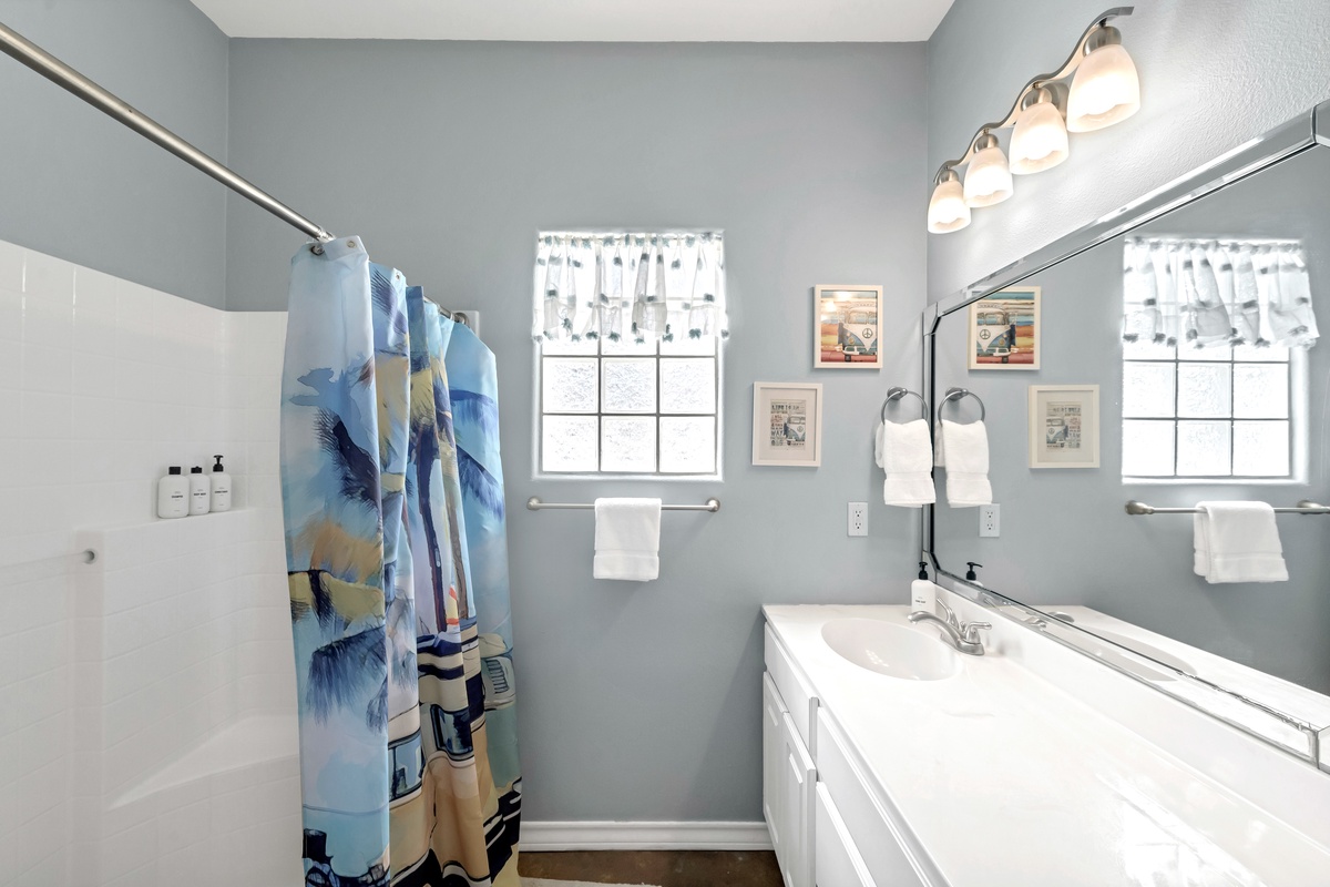 Step into your serene bathroom sanctuary with soft blue walls, bright vanity lighting, and beach-themed touches that set the perfect coastal mood.