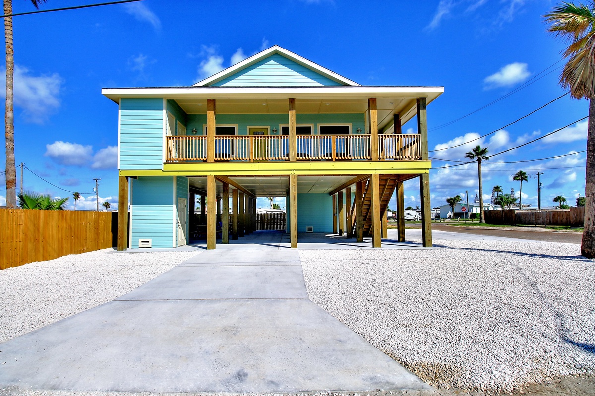 Charming turquoise beach house elevated on stilts with covered parking and tropical palm trees dotting the coastal neighborhood.