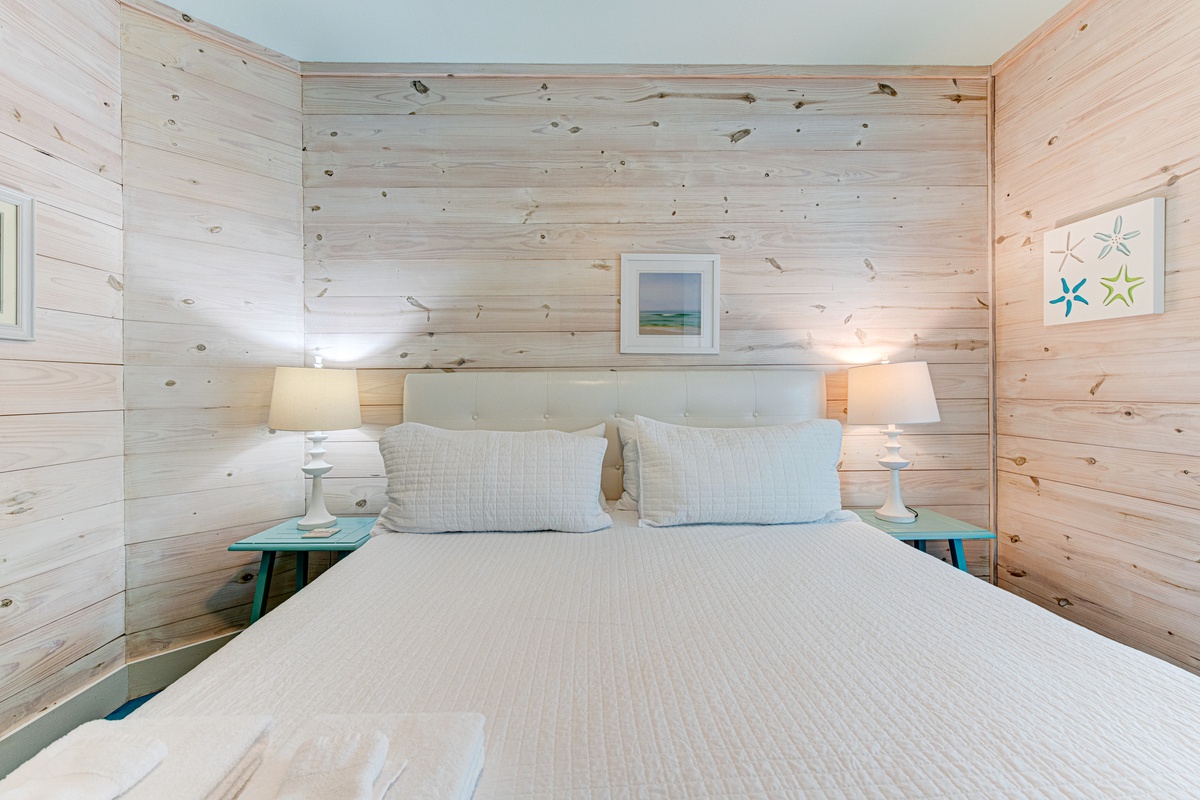 Drift off in this serene bedroom where whitewashed wood walls create a coastal haven, complemented by soft linens and gentle bedside lighting.