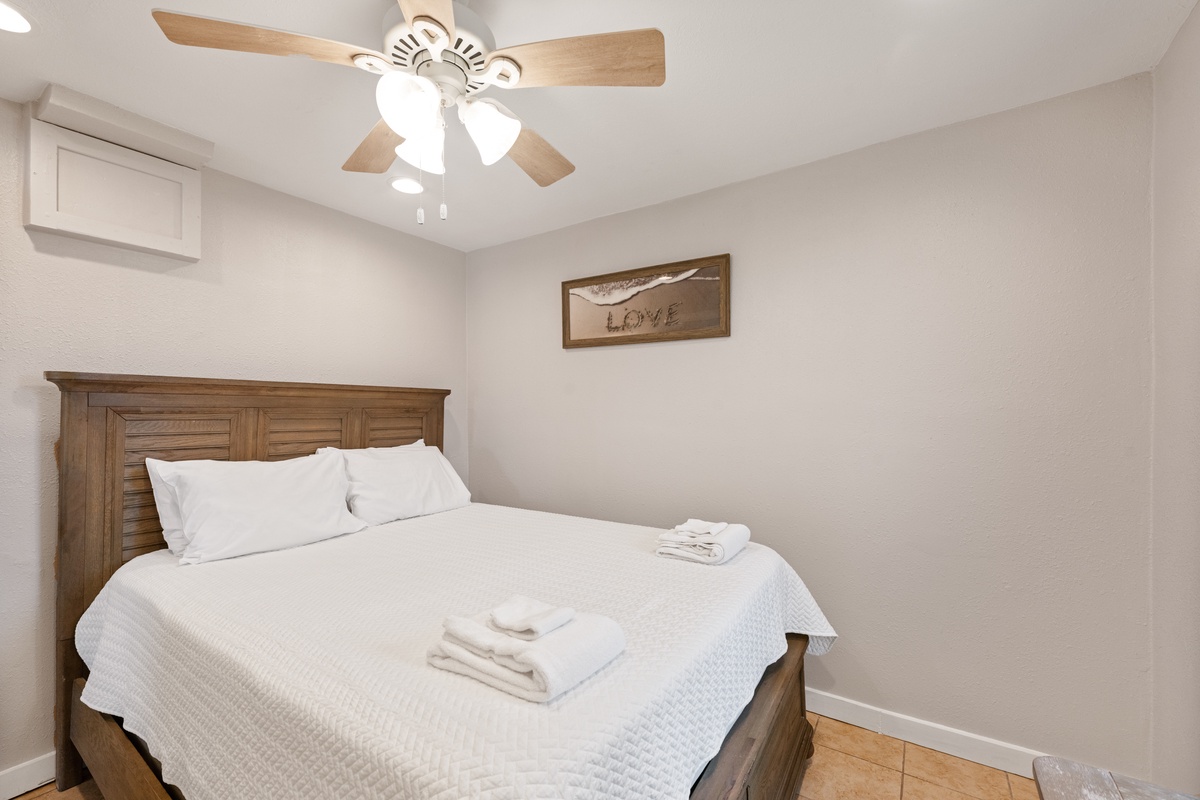 Sink into crisp white linens in your peaceful bedroom, where gentle ceiling fan breezes and warm wood touches create the perfect retreat.