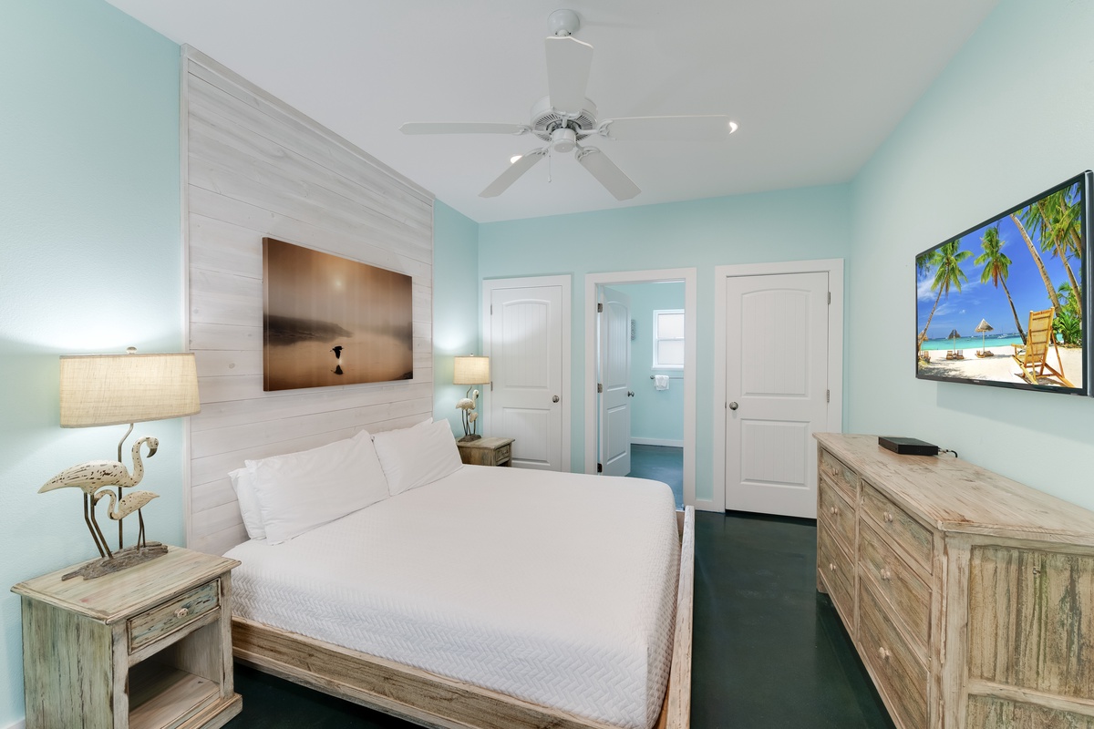 Drift off in your coastal-themed bedroom with aqua walls, ceiling fan comfort, and tropical artwork creating beach vibes.