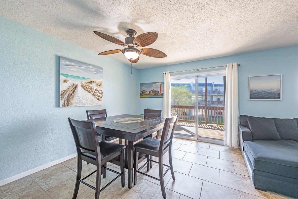 Savor meals in your coastal dining space with ocean artwork, tropical ceiling fan, and balcony access for dining al fresco.
