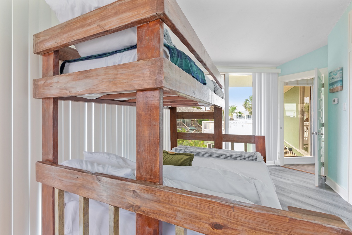 Your cozy wooden bunk beds offer comfort with crisp white linens, while bright windows frame tropical views for a perfect island retreat.