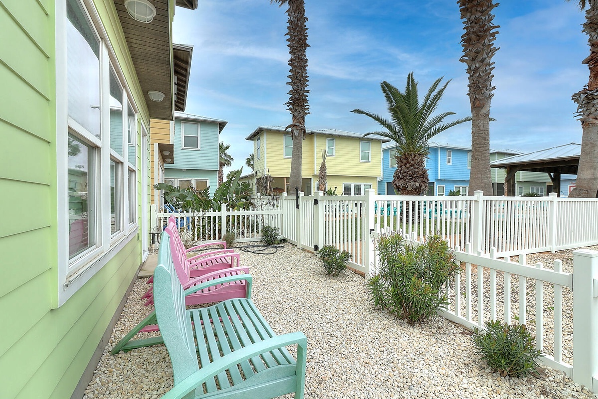 Relax on colorful chairs in your private yard surrounded by tropical palms and cheerful coastal homes.