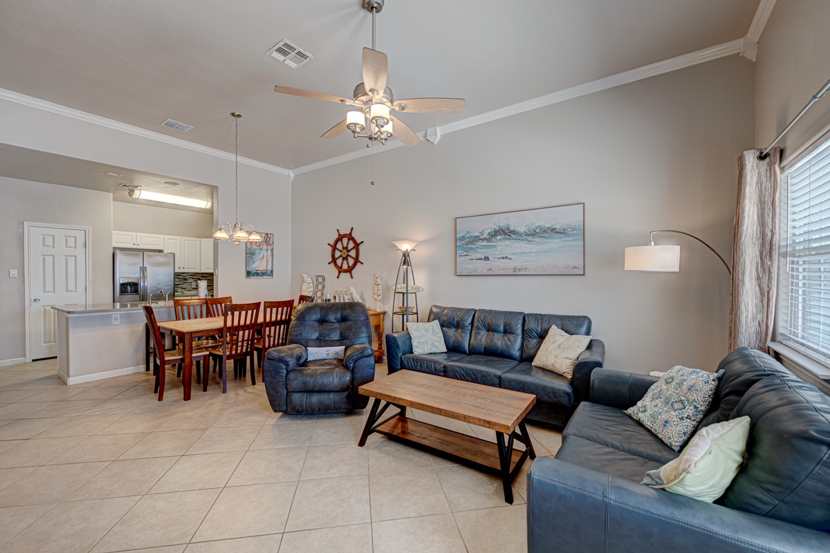 Relax in your spacious open-concept living area featuring plush leather seating, coastal décor, and a fully equipped kitchen perfect for family gatherings.