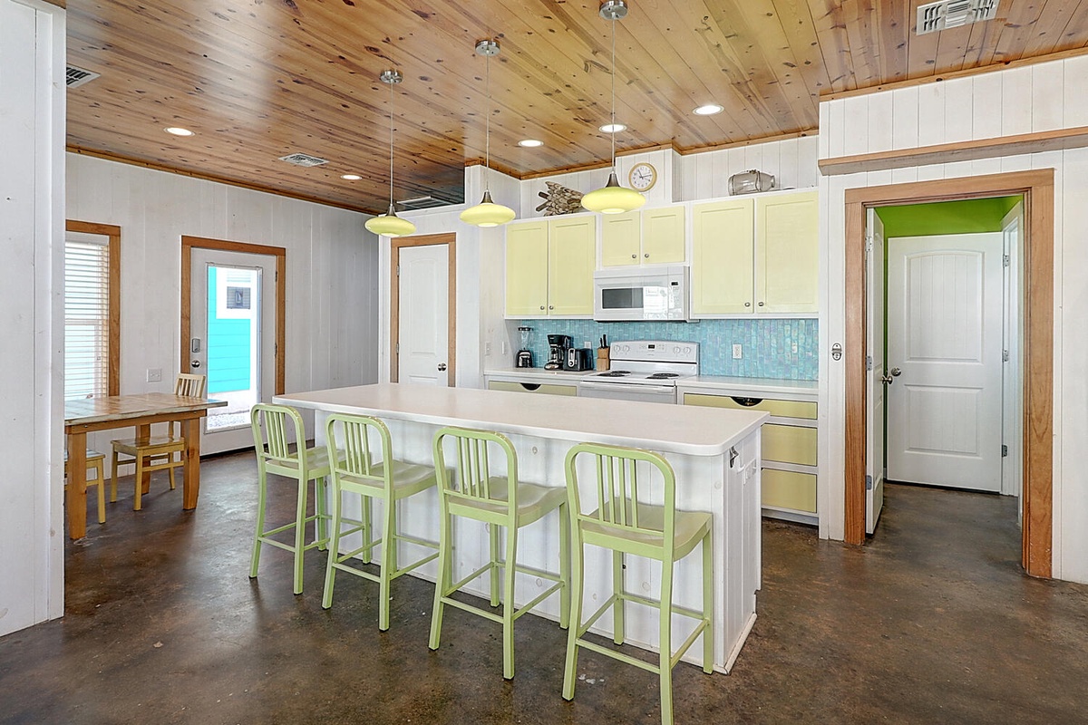 Your fully-equipped kitchen awaits with cheerful green accents, spacious island seating, and warm wood ceiling details creating the perfect gathering spot.