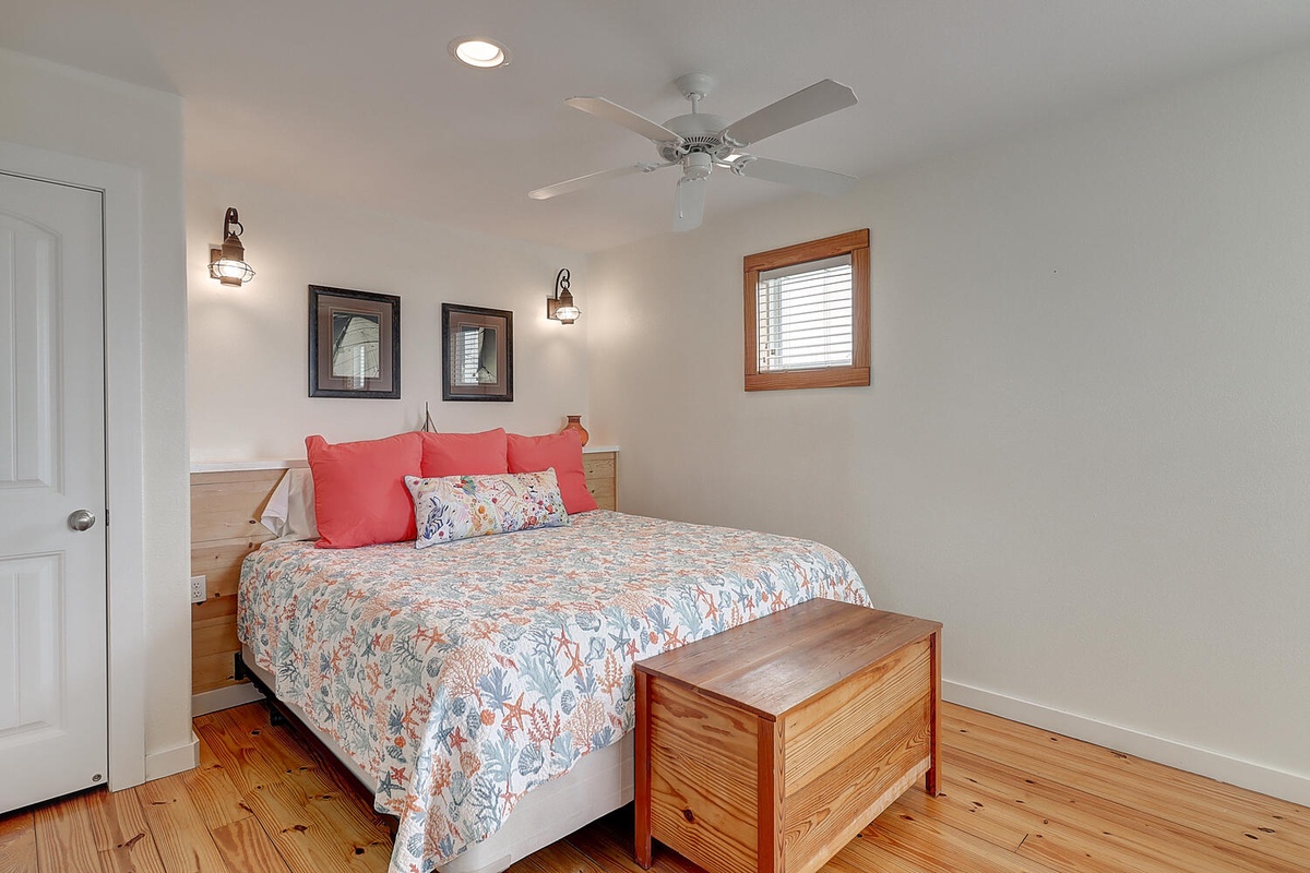 Settle into this cozy bedroom with coral accents, where gentle ceiling fan breezes and warm wood touches create your peaceful retreat.