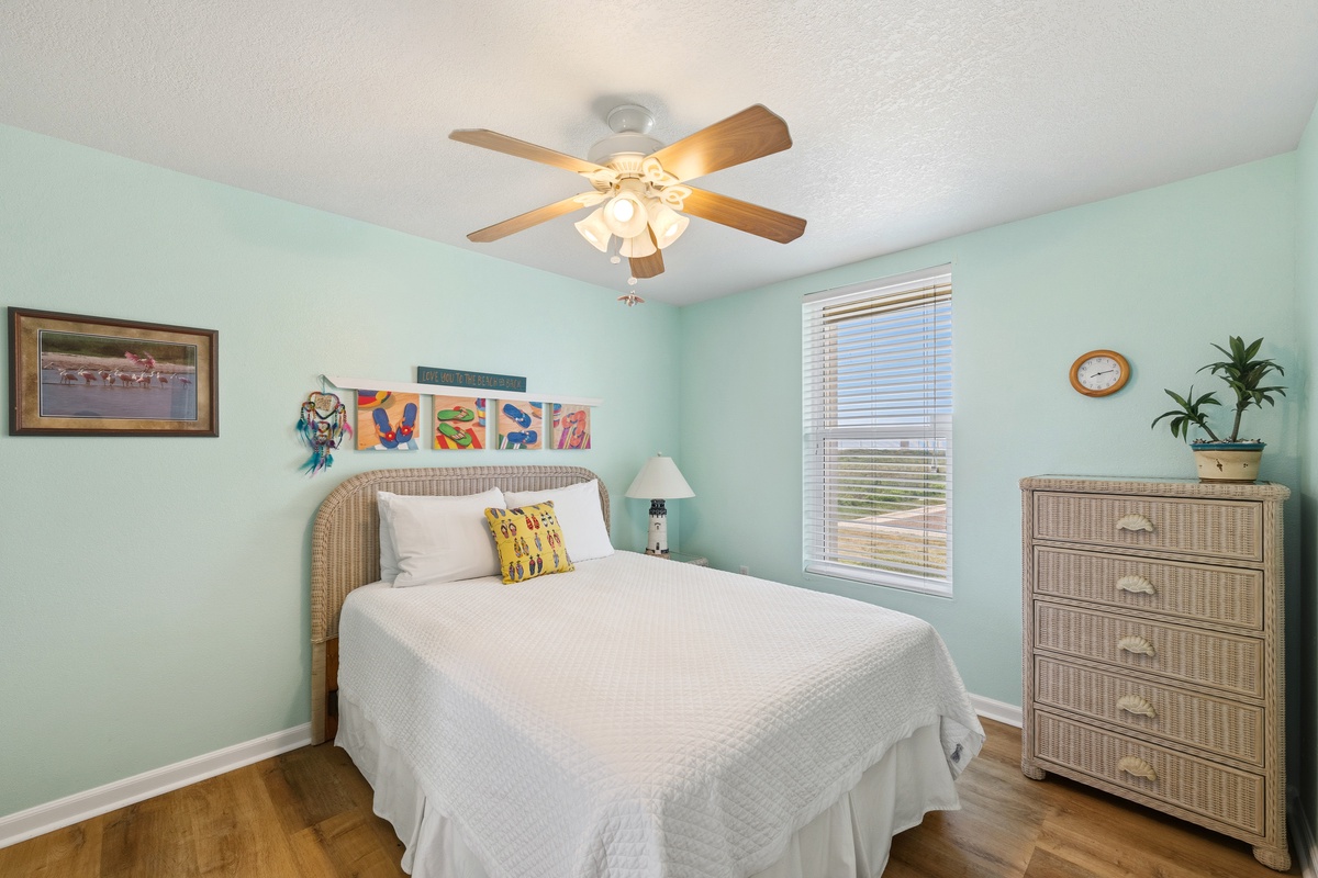 Drift off in your coastal-inspired bedroom, where soft mint walls and wicker furnishings create a serene retreat with natural hardwood floors beneath.