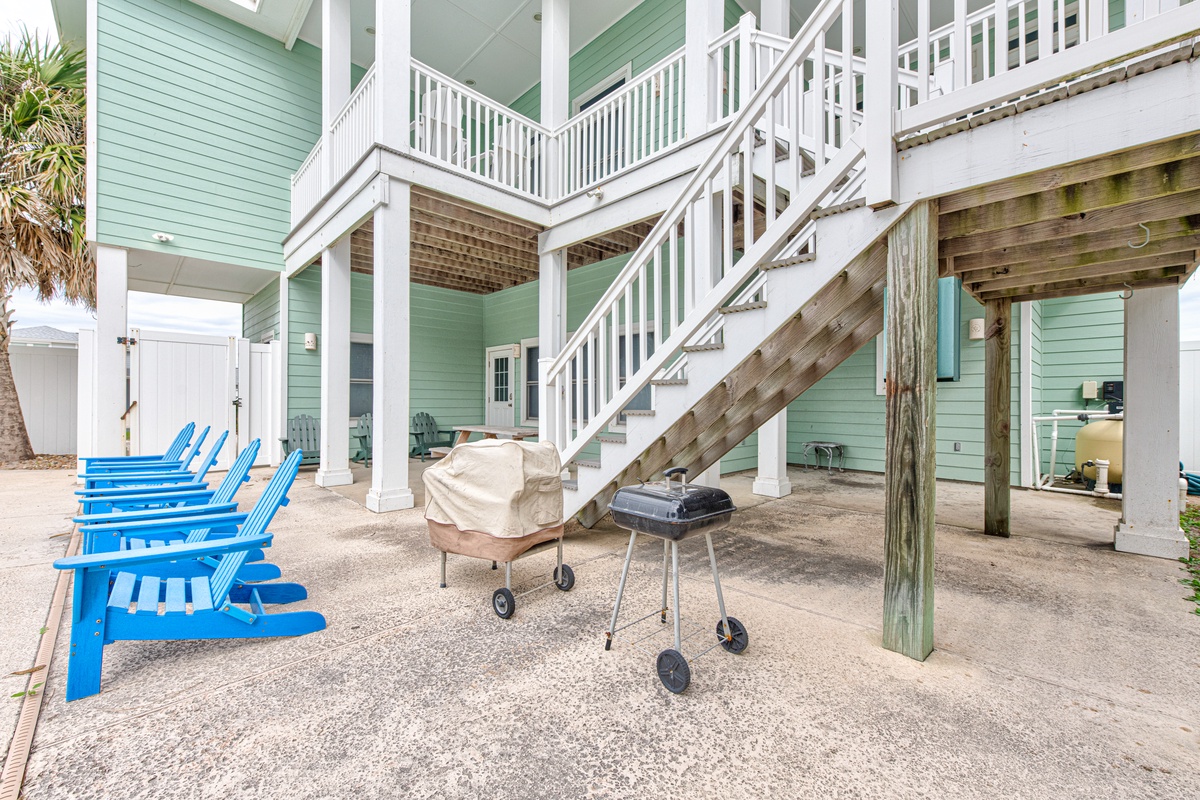 Your beach house getaway features a relaxing outdoor area with bright blue chairs and BBQ grill for memorable evenings together.