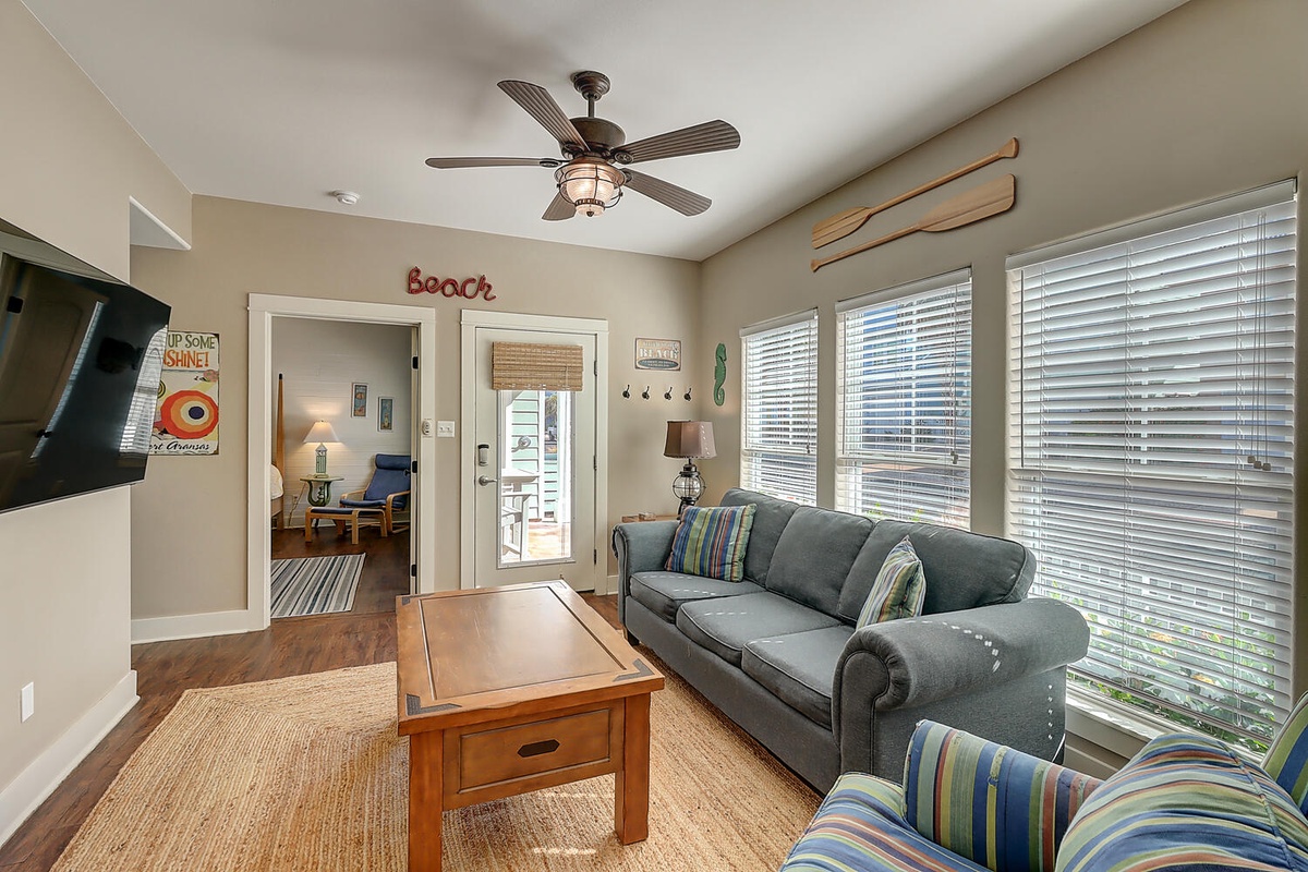 Relax in your bright living room with comfy seating, beach-themed décor, and natural light streaming through large windows.