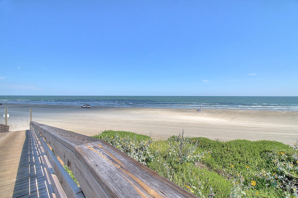 Pristine coastline stretches endlessly with sandy shores meeting azure waters under clear skies.