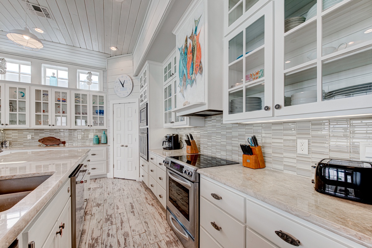 You'll love cooking in this bright, coastal-inspired kitchen with gleaming white cabinets, premium appliances, and charming glass-front storage for your beach getaway essentials.
