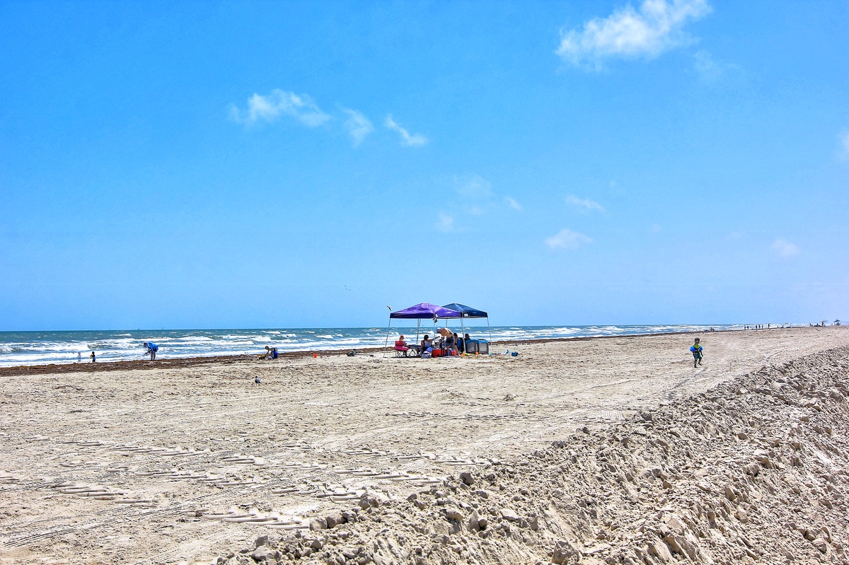 Miles of pristine sandy coastline stretch endlessly under brilliant blue skies, with gentle waves and scattered beachgoers enjoying the peaceful atmosphere.