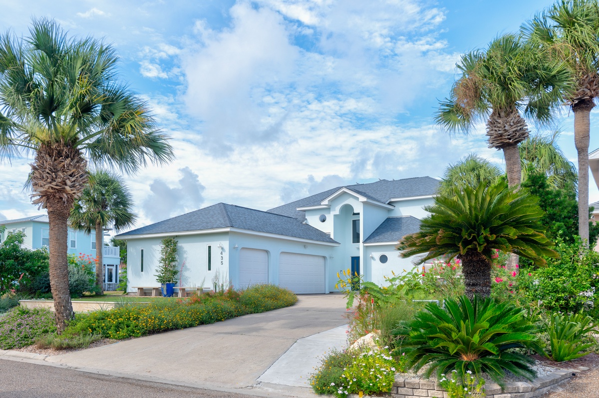 A spacious two-story home framed by swaying palms and lush tropical landscaping, offering a welcoming coastal retreat in a serene neighborhood.