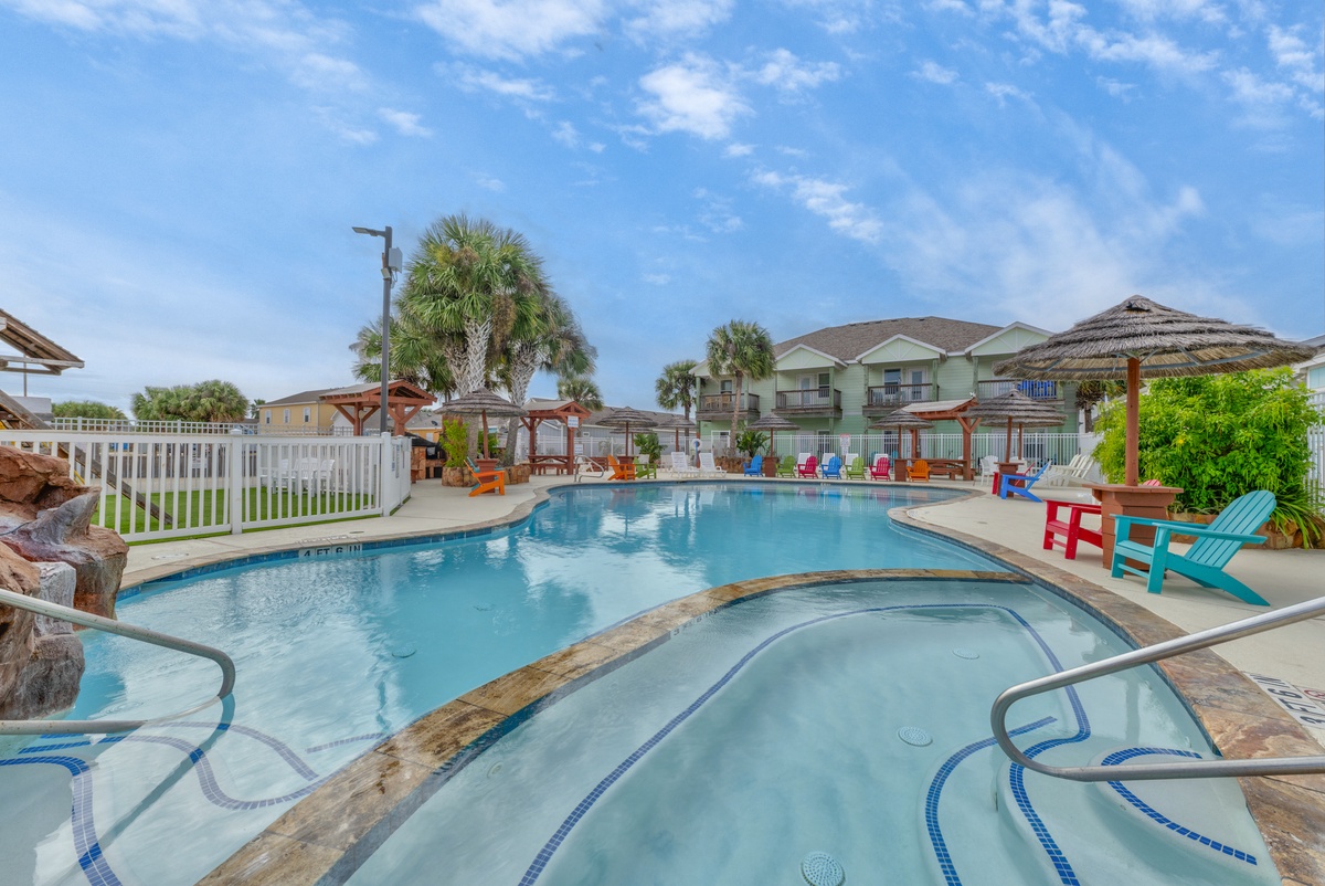 Bright tropical pool area with hot tub, colorful chairs, and palm trees under blue skies at this beachside resort.
