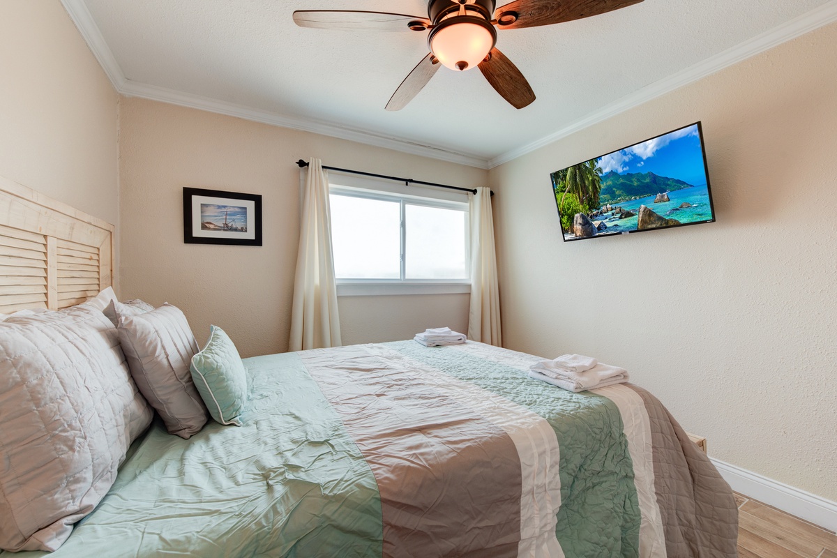 Unwind in your serene bedroom featuring a plush king bed, ceiling fan for comfort, and wall-mounted TV for relaxation.
