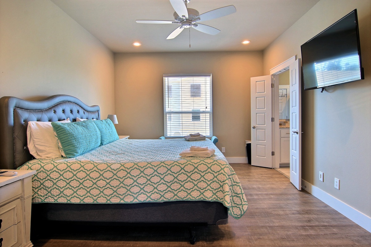 Unwind in your elegant bedroom featuring a plush tufted headboard, soothing coastal colors, and modern amenities including a wall-mounted TV for ultimate relaxation.