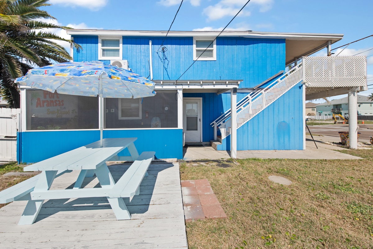 Bright blue beach house with covered outdoor dining and palm tree shade for perfect coastal relaxation.