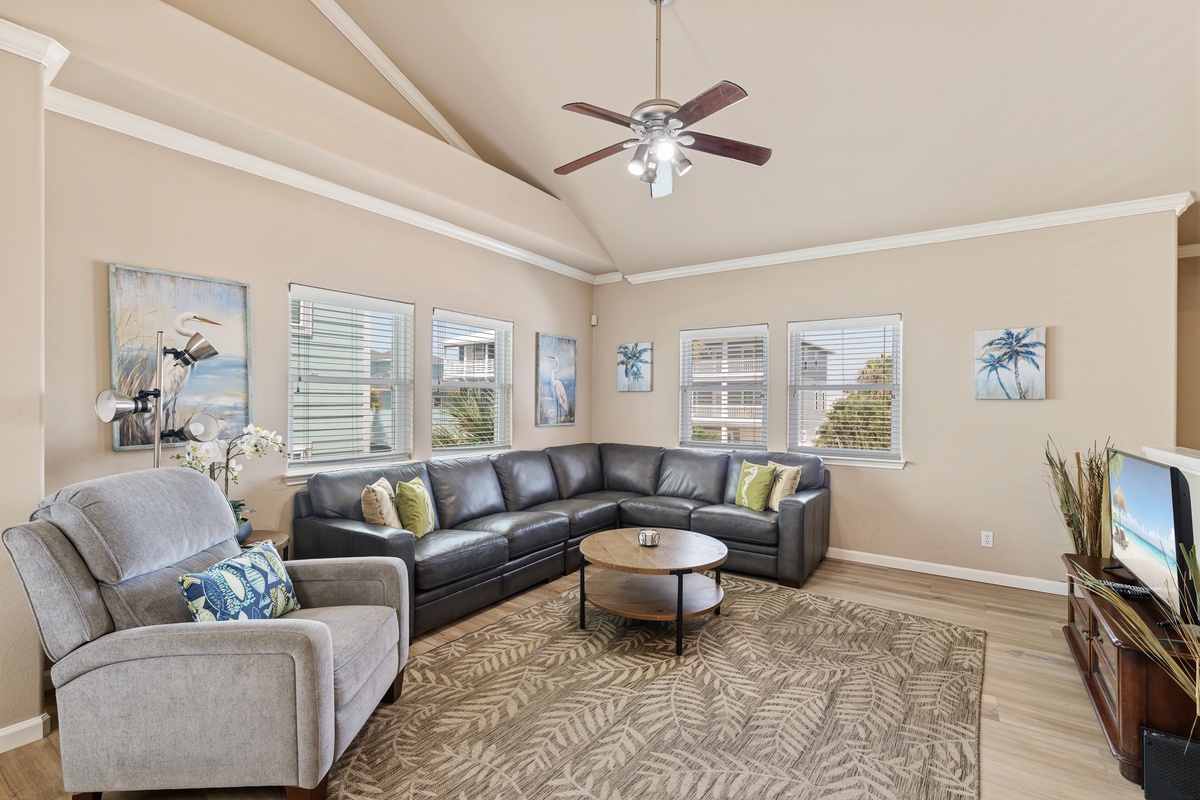 Relax in a bright and spacious living room featuring comfortable seating, coastal-inspired décor, and large windows that fill the space with natural light.