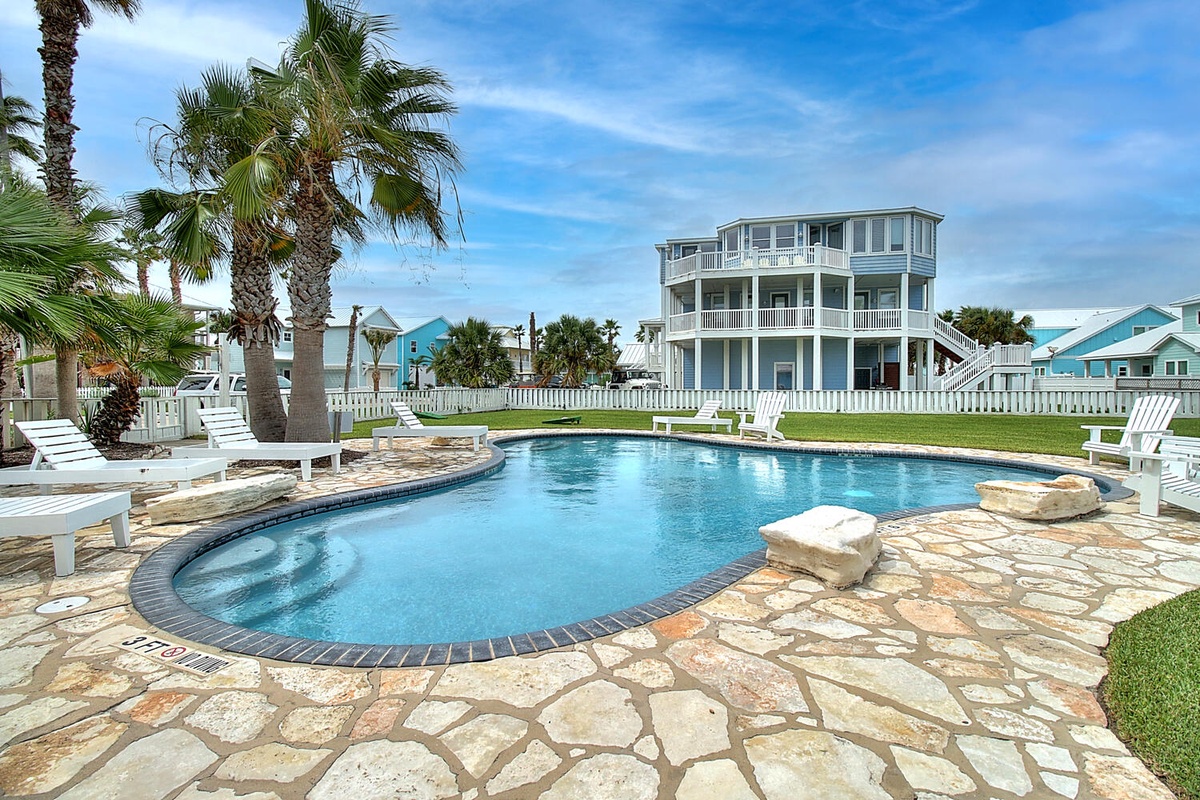 Stunning coastal vacation home with private pool, tropical palms, and elegant three-story design featuring multiple balconies and beach house charm.