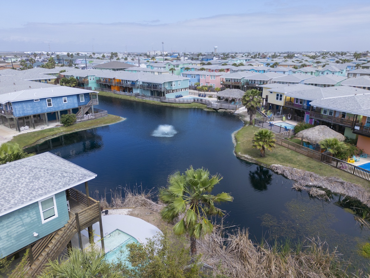 Aerial view of the property situated within a vibrant waterfront neighborhood, featuring colorful beach homes surrounding a peaceful canal with palm-lined shores and coastal charm.