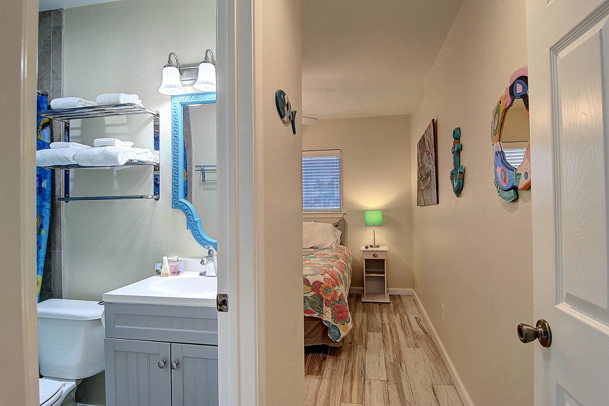 Your cozy retreat features a bright bathroom and comfortable bedroom with tropical wall art and warm wood floors.