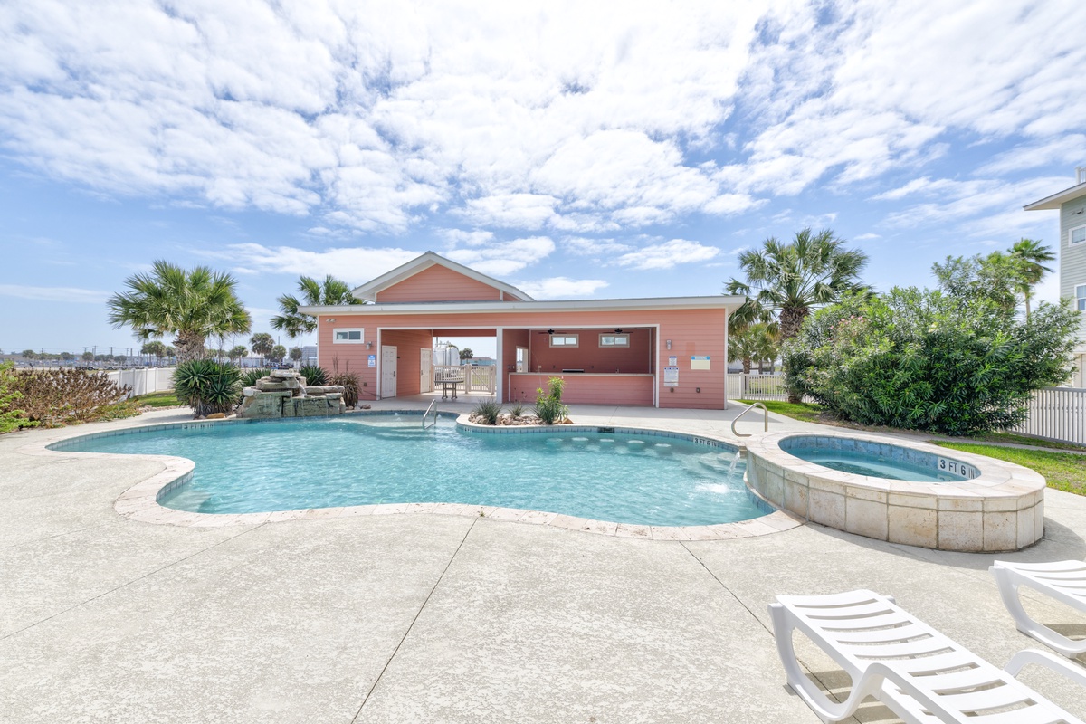Beautiful swimming pool with hot tub surrounded by palm trees and tropical landscaping under sunny skies.