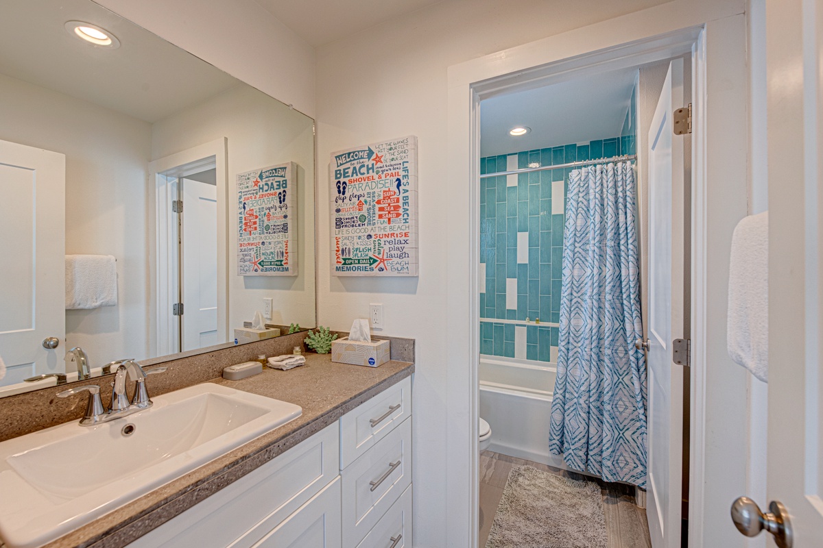 Your bright bathroom features dual vanities and a vibrant teal-tiled tub perfect for unwinding after beach days.