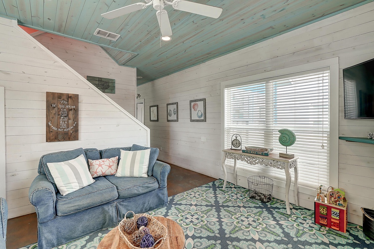 Relax in your charming living space with coastal blue ceiling, comfy sofa, and peaceful window views.
