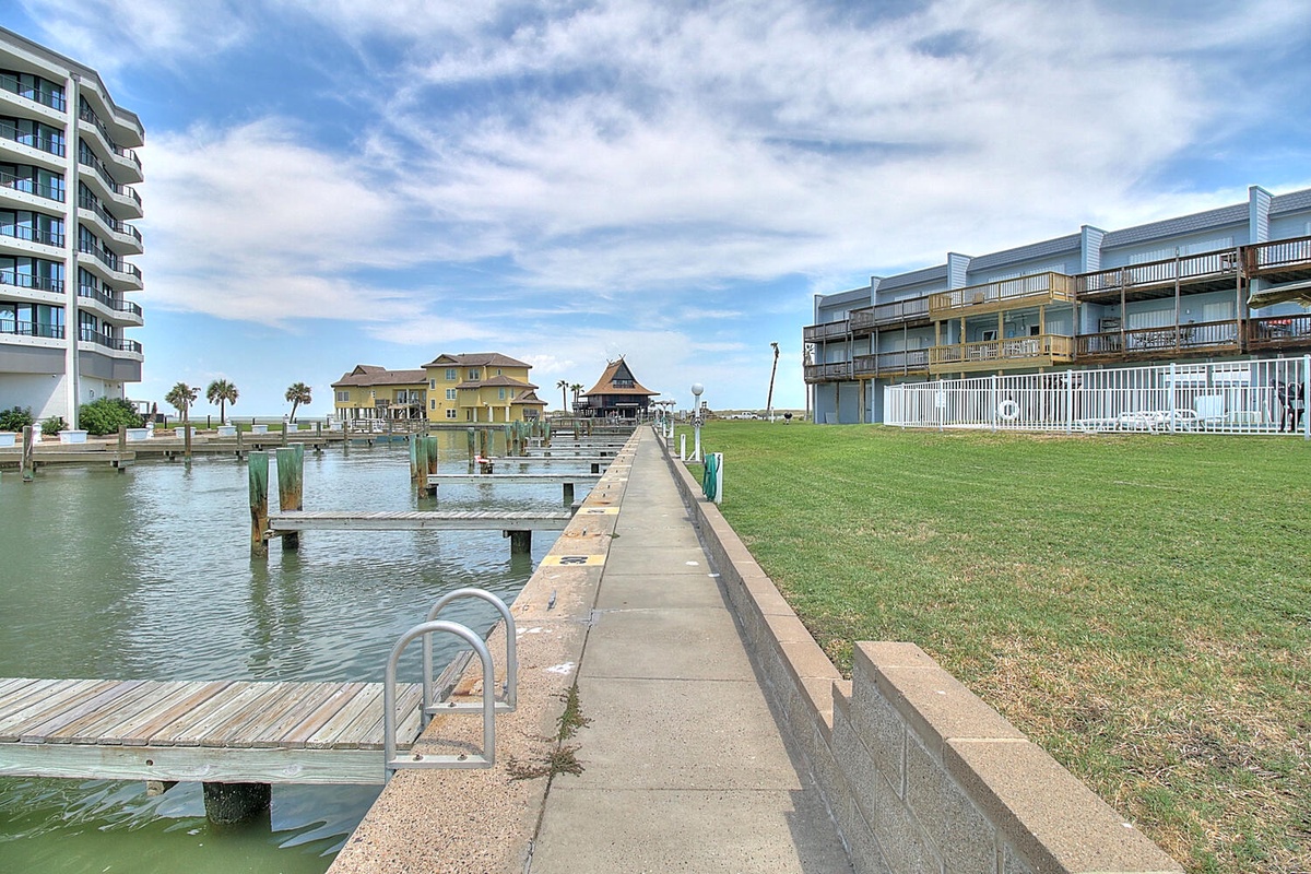 Waterfront resort property featuring a private fishing pier extending into calm bay waters, surrounded by modern vacation buildings and manicured grounds.