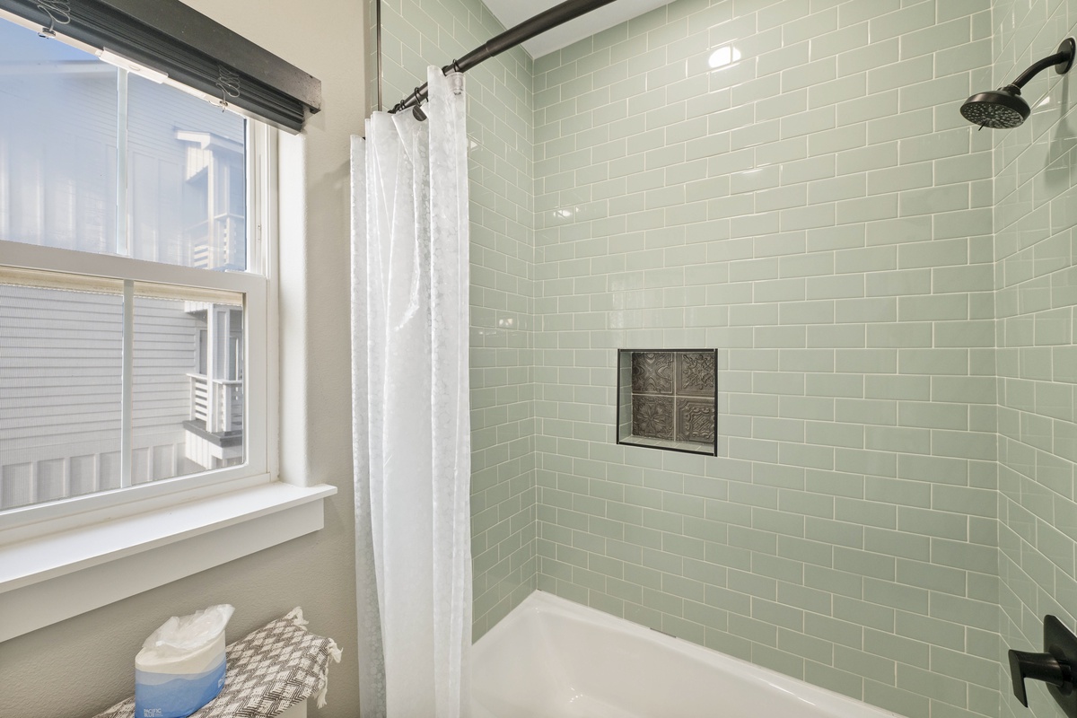 Unwind in your elegant bathroom featuring a soothing mint-green tiled shower and bright natural light streaming through the window.