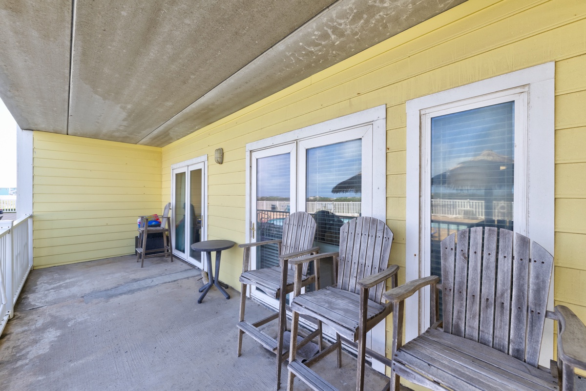 Your private covered balcony features weathered Adirondack chairs and a small bistro table, perfect for morning coffee or evening relaxation with coastal breezes and glimpses of the surrounding area.