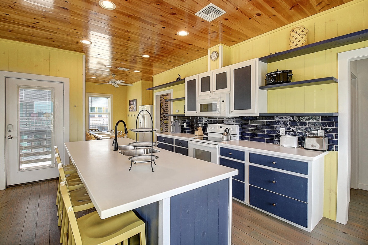 Your spacious kitchen invites culinary adventures with gleaming countertops, modern appliances, and vibrant blue cabinetry under warm wood ceilings.