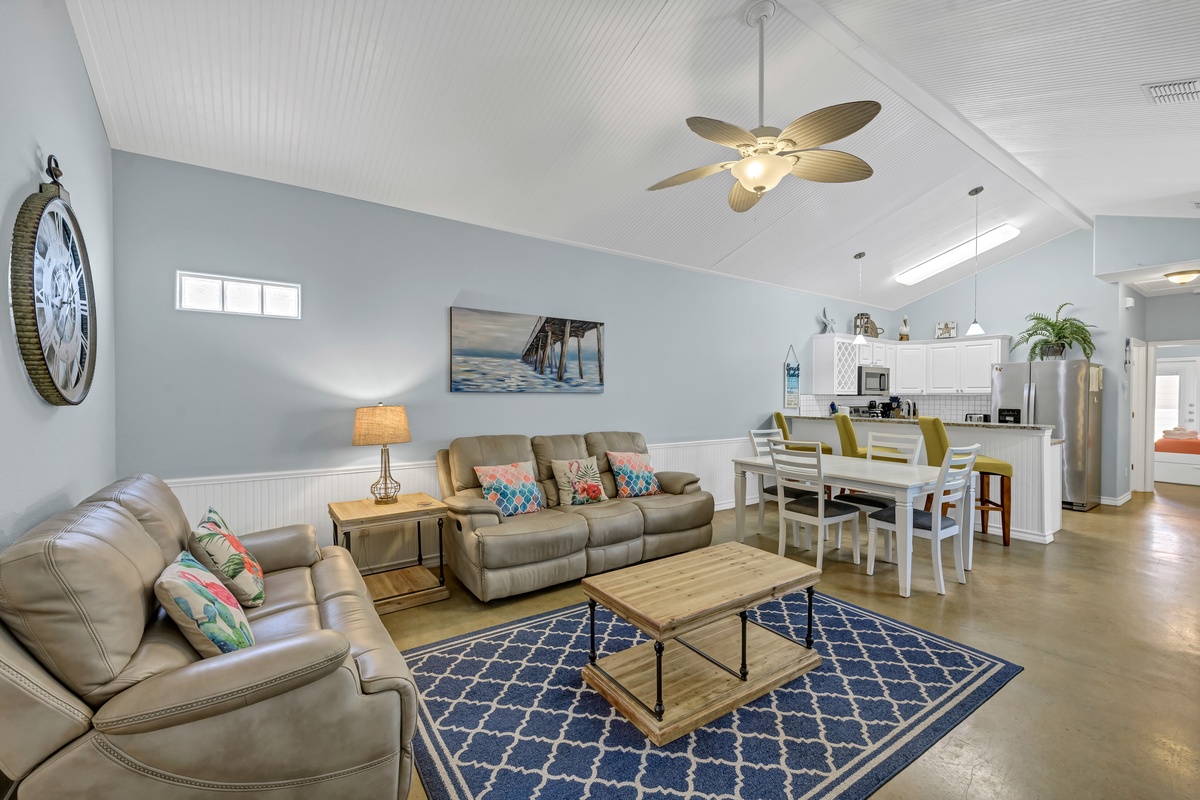 Relax in your spacious living room with plush leather seating, coastal decor, and an open kitchen perfect for vacation memories.