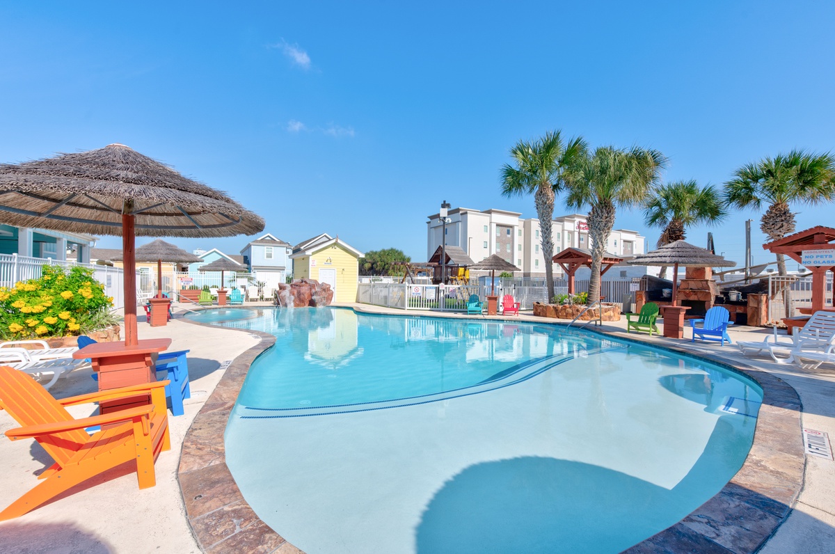 Dive into tropical bliss with this sparkling pool surrounded by vibrant beach huts and swaying palms—your perfect coastal getaway awaits.