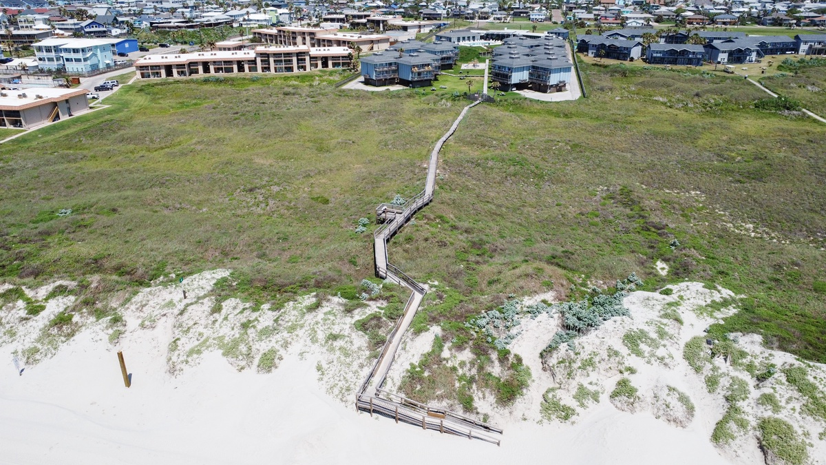Aerial view of beachfront location showing wooden walkway connecting residential neighborhood to pristine sandy shore.